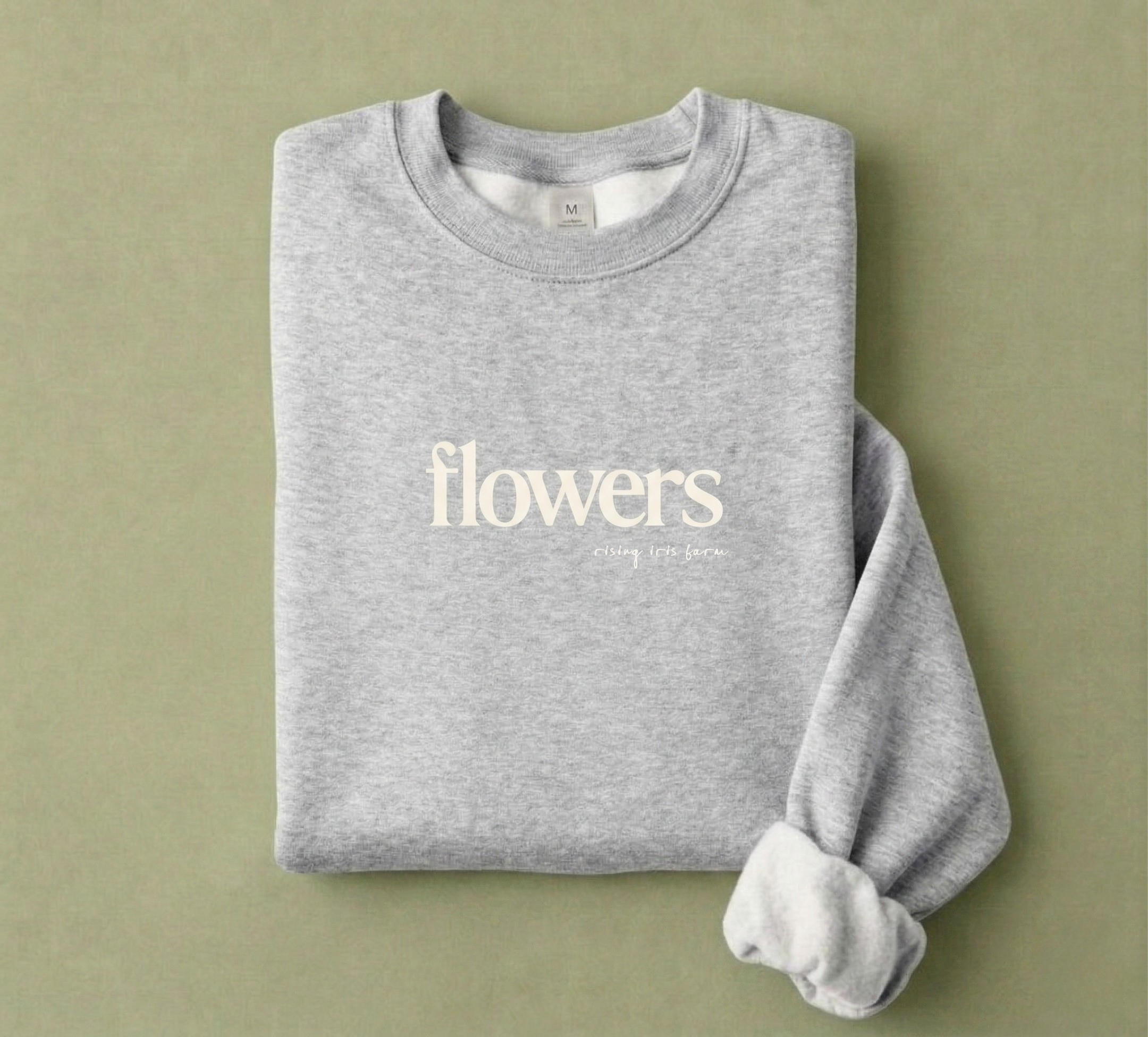 Folded gray sweatshirt with 'flowers' text on a green background