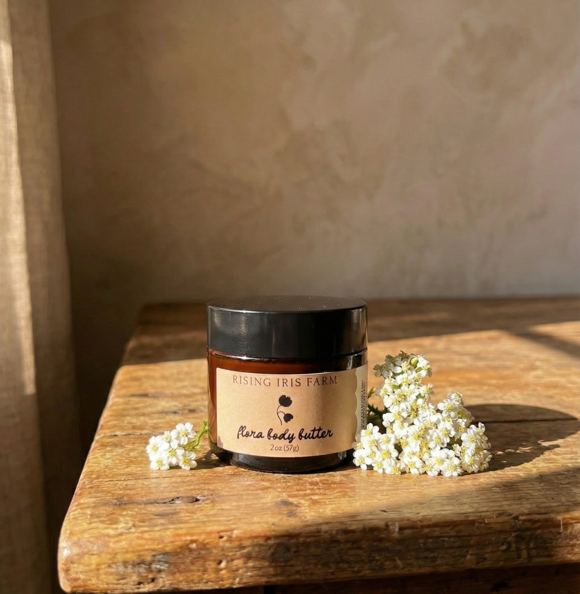 Jar of Rising Iris Farm flora body butter on a wooden surface with white flowers.