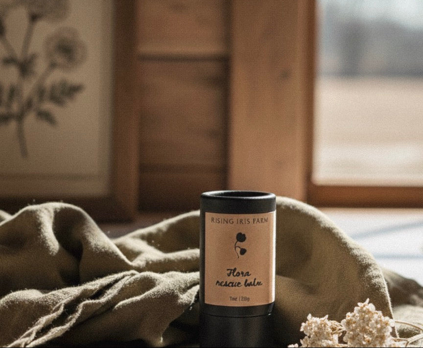 Black cylindrical container with a label on a wooden surface with a cloth and flowers.
